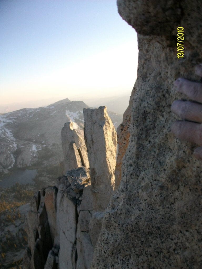 Kyle Khalil's hand touches a spire of granite that spills forward into subsequent spires atop the high elevation summit of Cathedral Peak, the view below drops several hundred feet into the Tuolumne high country below. 