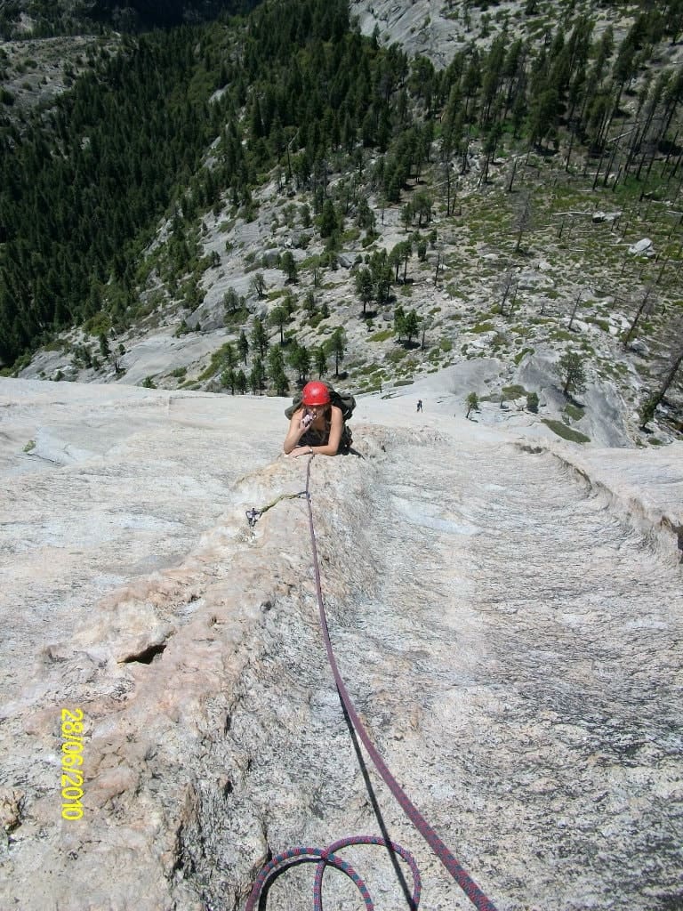 Kyle Khalil hundreds of feet off the ground on a granite dike that ascends Half Dome. A rope trails above her as she pauses to hydrate.